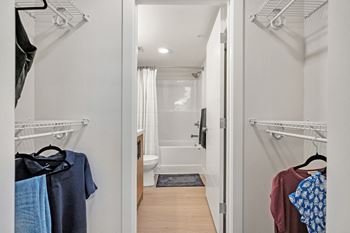 A walk in closet with clothes hanging on the wall and a bathroom in the background